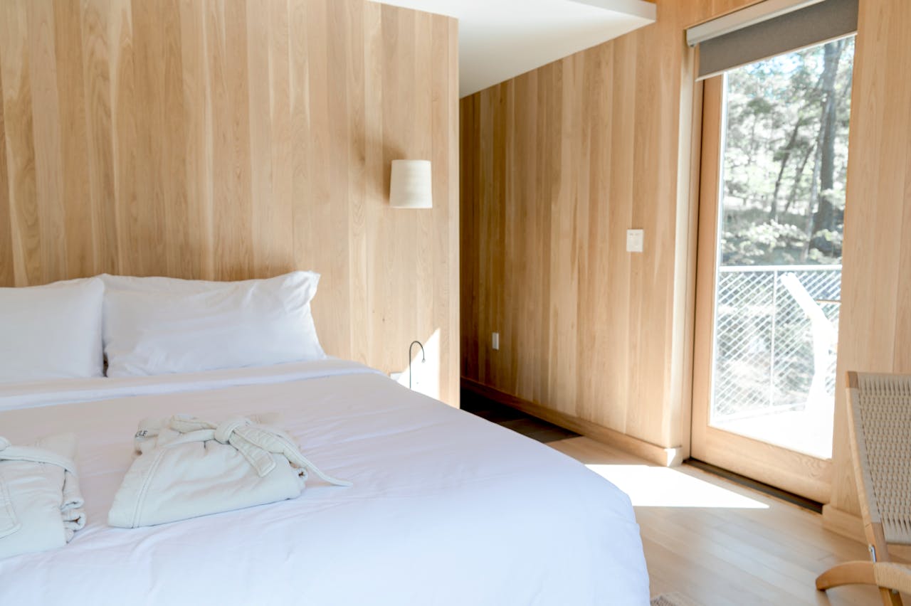 Bright minimalist bedroom with large windows, wooden walls, and a cozy bed, offering a peaceful retreat.