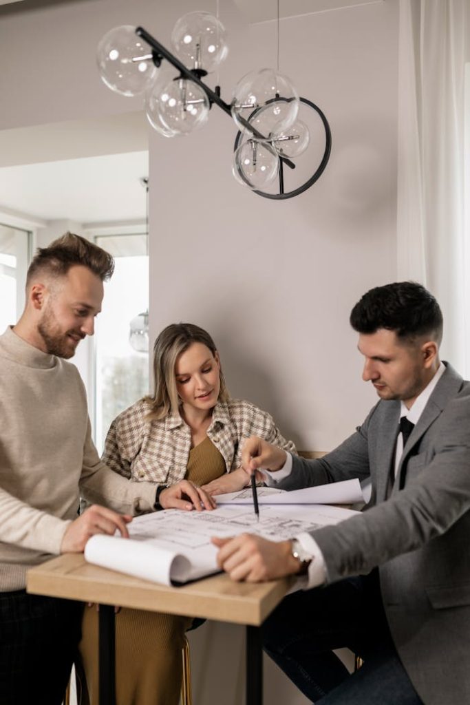 Couple discussing a blueprint with a real estate agent, planning their new home purchase.